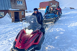 снегоход тянет нарты с туристами зимой