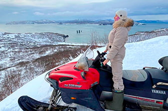 смотрит вдаль на океан со снегохода
